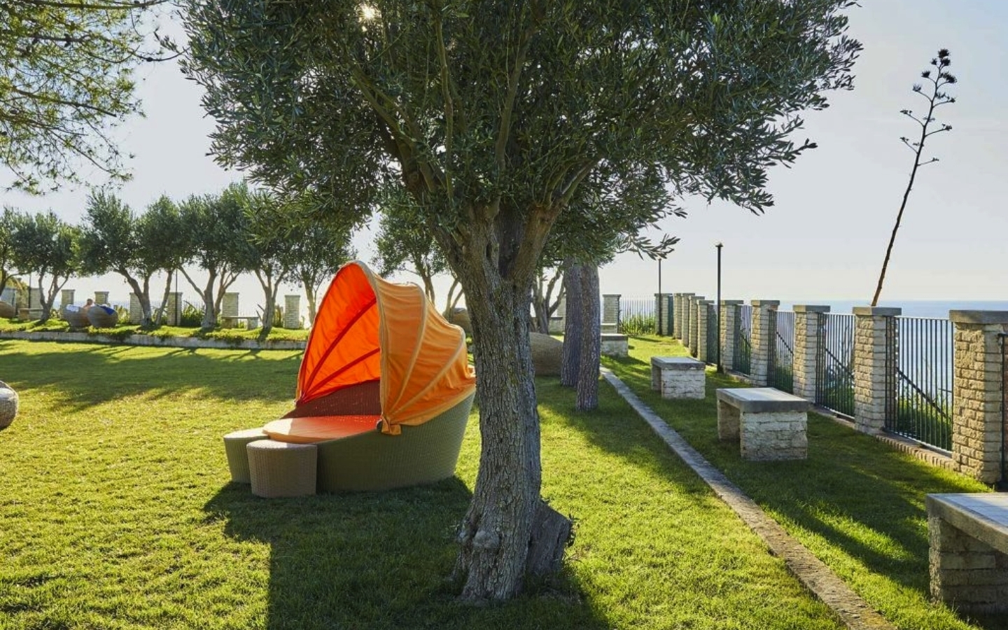 Gartenbereich mit Liege und Sonnensegel, umgeben von Bäumen und gemauerten Zäunen.