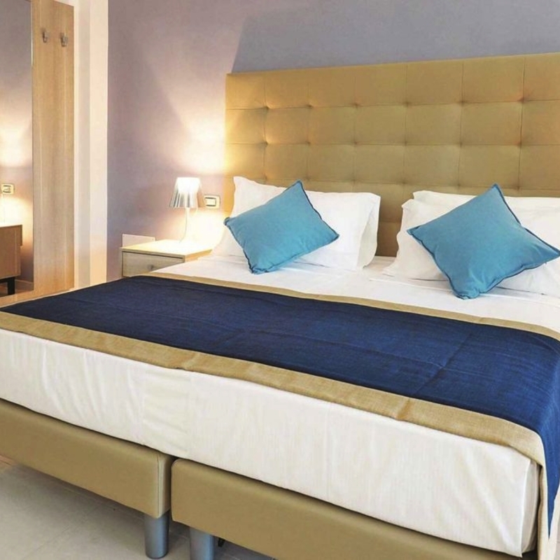 Doppelzimmer mit Bett, Nachttischen und Lampe in neutralen Farben.