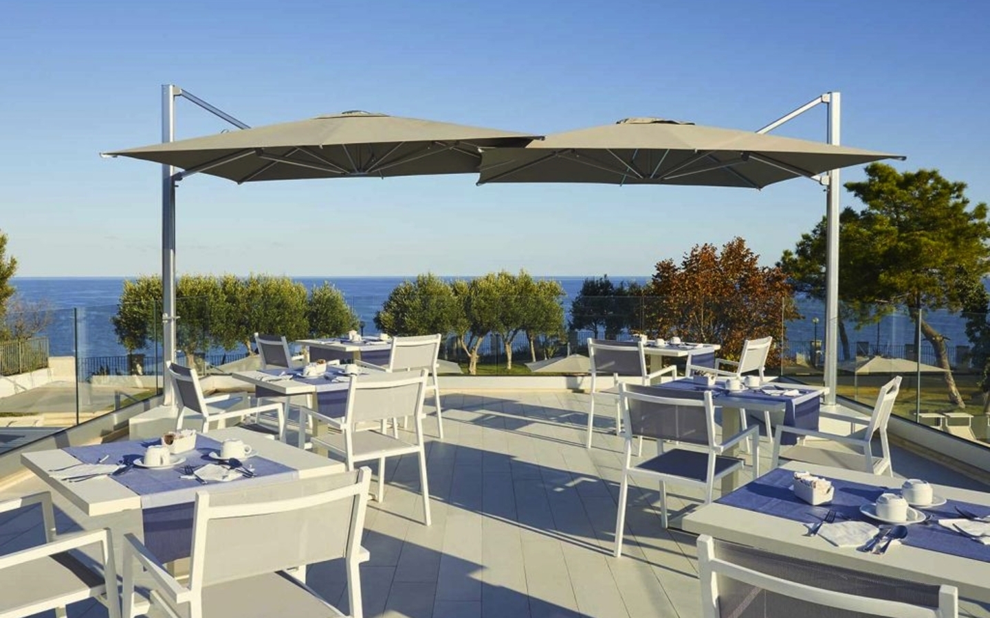 Außenterrasse eines Hotels mit Meerblick und Tischen unter Sonnenschirmen.