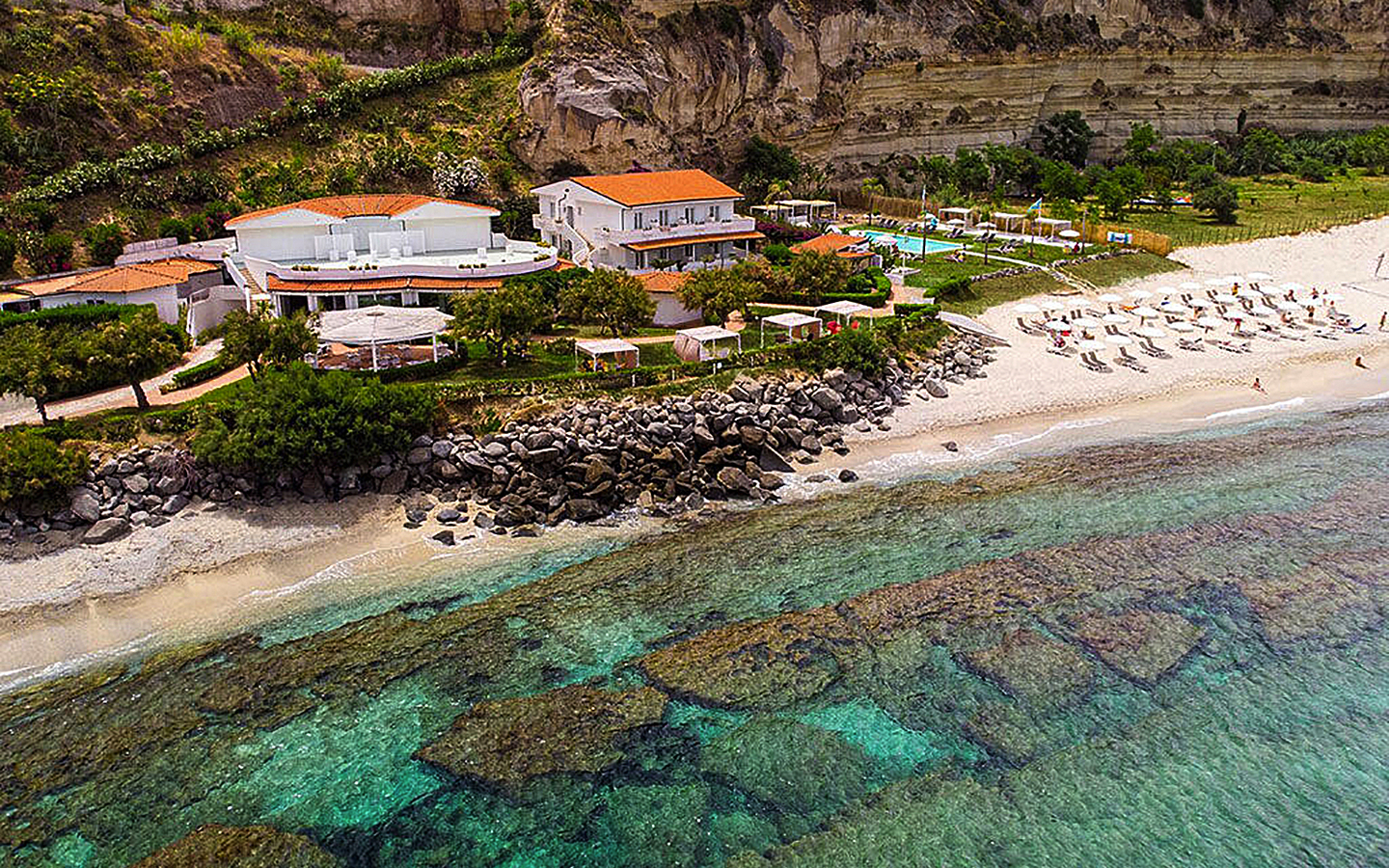 Luftaufnahme des Borgo di Riaci Resorts in Kalabrien mit Strand und klarem Wasser.