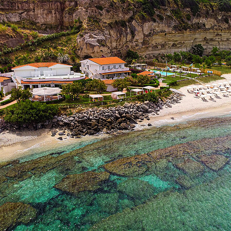 Luftaufnahme des Borgo di Riaci Resorts in Kalabrien mit Strand und klarem Wasser.
