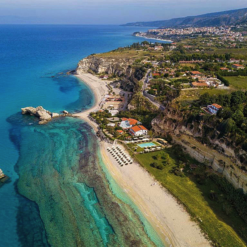 Luftaufnahme von Strand und Küste in Kalabrien, Italien, mit Resort und Klippen.