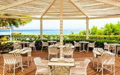 Terrasse eines Restaurants mit weißen Tischen und Stühlen, Blick aufs Meer.
