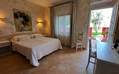 Hotelzimmer mit Doppelbett, Stuhl, Fenster und Terrassentür mit Blick auf Garten.