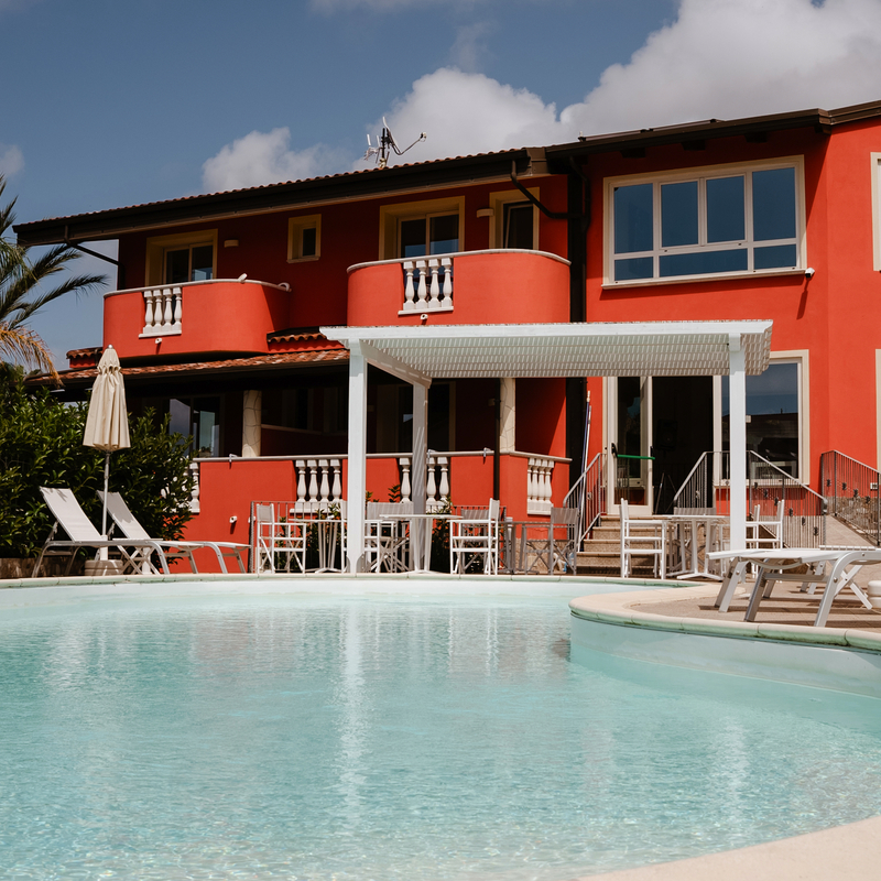 Hotel mit Pool in Kalabrien, Italien, umgeben von Liegestühlen und Sonnenschirmen.