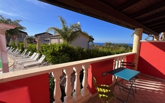 Blick von einem Balkon auf Palmen, Liegestühle und das Meer in Kalabrien, Italien.