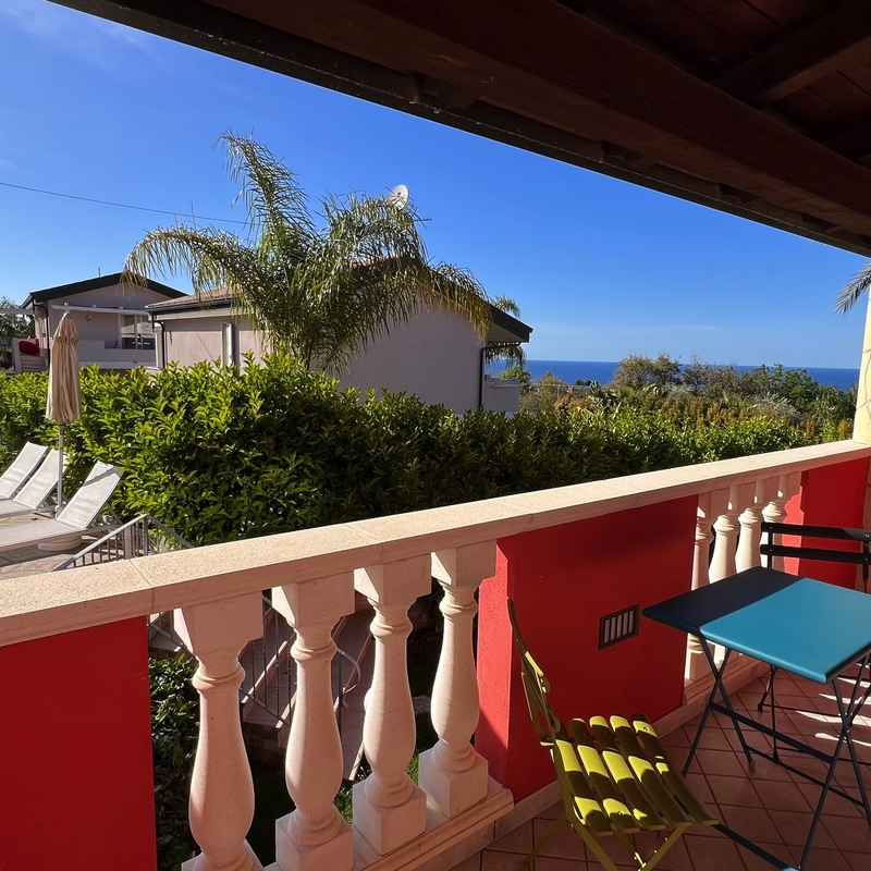 Blick von einem Balkon auf Palmen, Liegestühle und das Meer in Kalabrien, Italien.