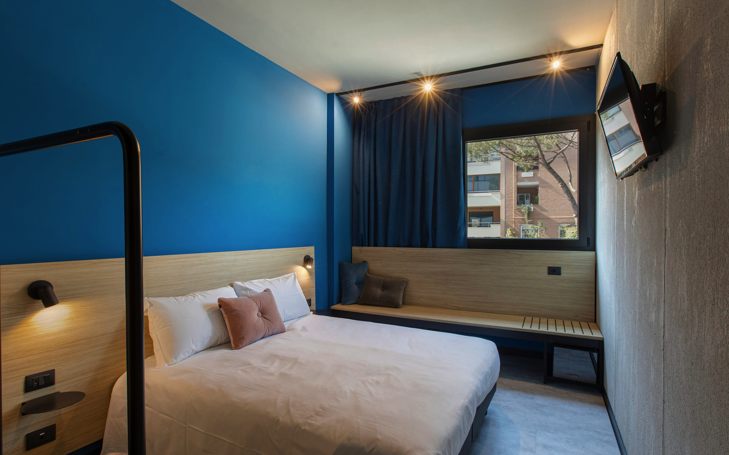 Modern eingerichtetes Hotelzimmer mit Bett, blauem Akzent und Wand-TV.