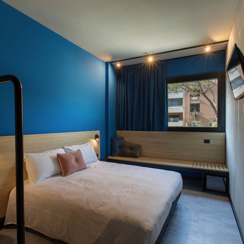 Modern eingerichtetes Hotelzimmer mit Bett, blauem Akzent und Wand-TV.