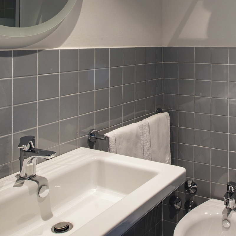 Badezimmer mit Waschbecken, Spiegel und grauen Kacheln im Hotel Ibis Styles Roma Aurelia.