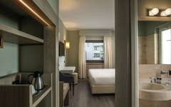 Hotelzimmer mit Doppelbett, Schreibtisch, Sessel und ein helles Badezimmer.