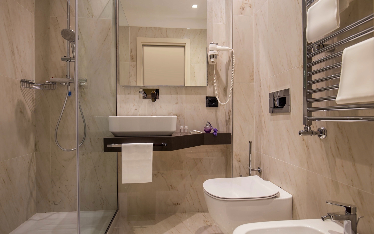 Modernes Hotelbadezimmer mit Dusche, WC, Waschbecken und Handtuchhalter.