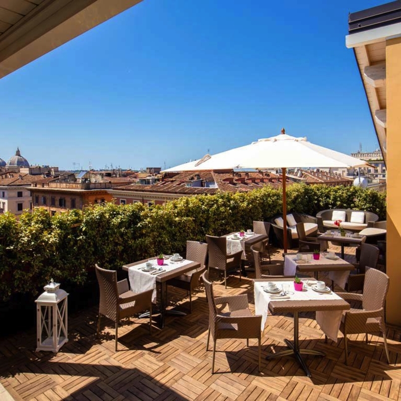 Terrasse des Hotel Gioberti in Rom mit Tischen und Sonnenschirmen, Blick auf die Stadt.