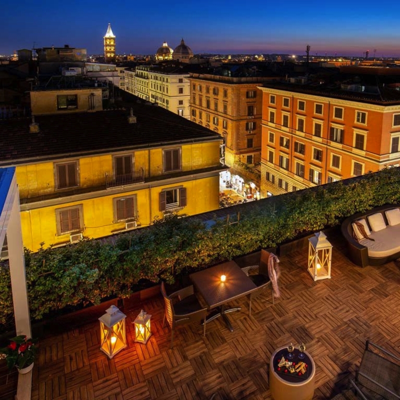 Blick von einer Terrasse bei Nacht auf beleuchtete Gebäude in Rom.