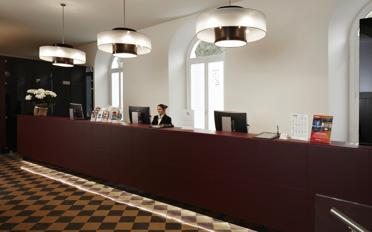 Hotelrezeption mit langen roten Tresen, Lampen und einem Empfangsmitarbeiter.