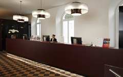 Hotelrezeption mit langen roten Tresen, Lampen und einem Empfangsmitarbeiter.