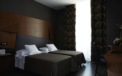 Modernes Hotelzimmer mit zwei Einzelbetten, dunklem Dekor und großen Vorhängen.