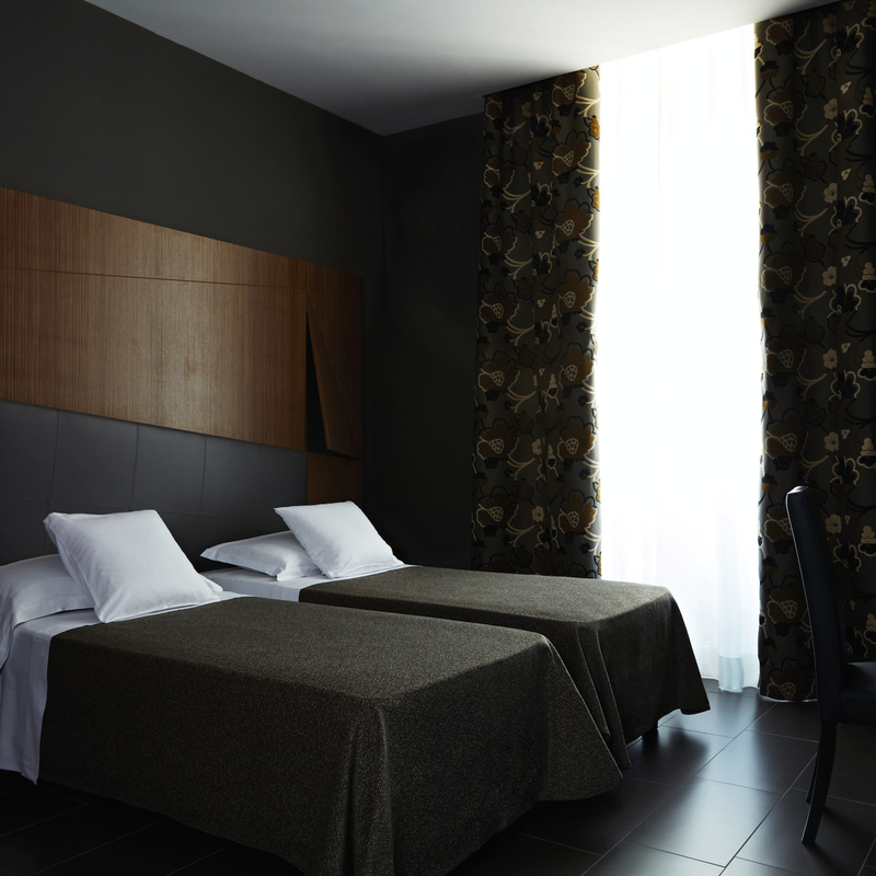 Modernes Hotelzimmer mit zwei Einzelbetten, dunklem Dekor und großen Vorhängen.