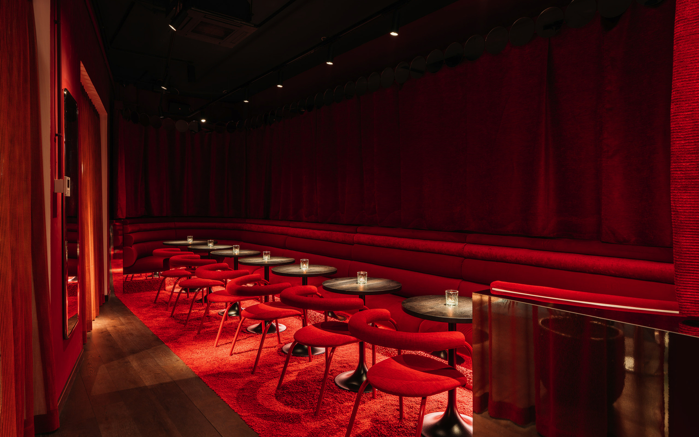 Elegante Hotelbar mit roten Vorhängen, Tischen und Stühlen.