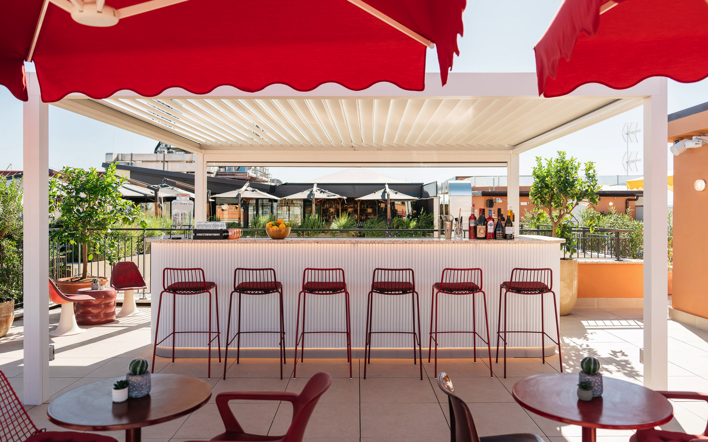Eine Hotelterrasse mit roten Stühlen und Bar vor Sonnenschutz.