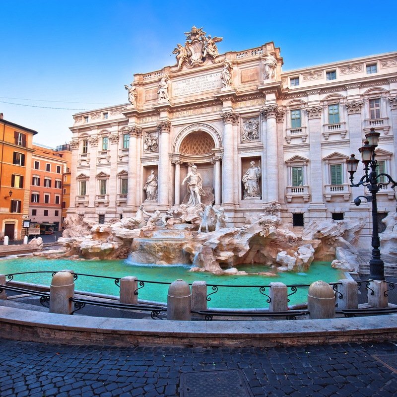 Barockbrunnen in Stadtplatz mit großen Skulpturen und umgebenden Gebäuden.