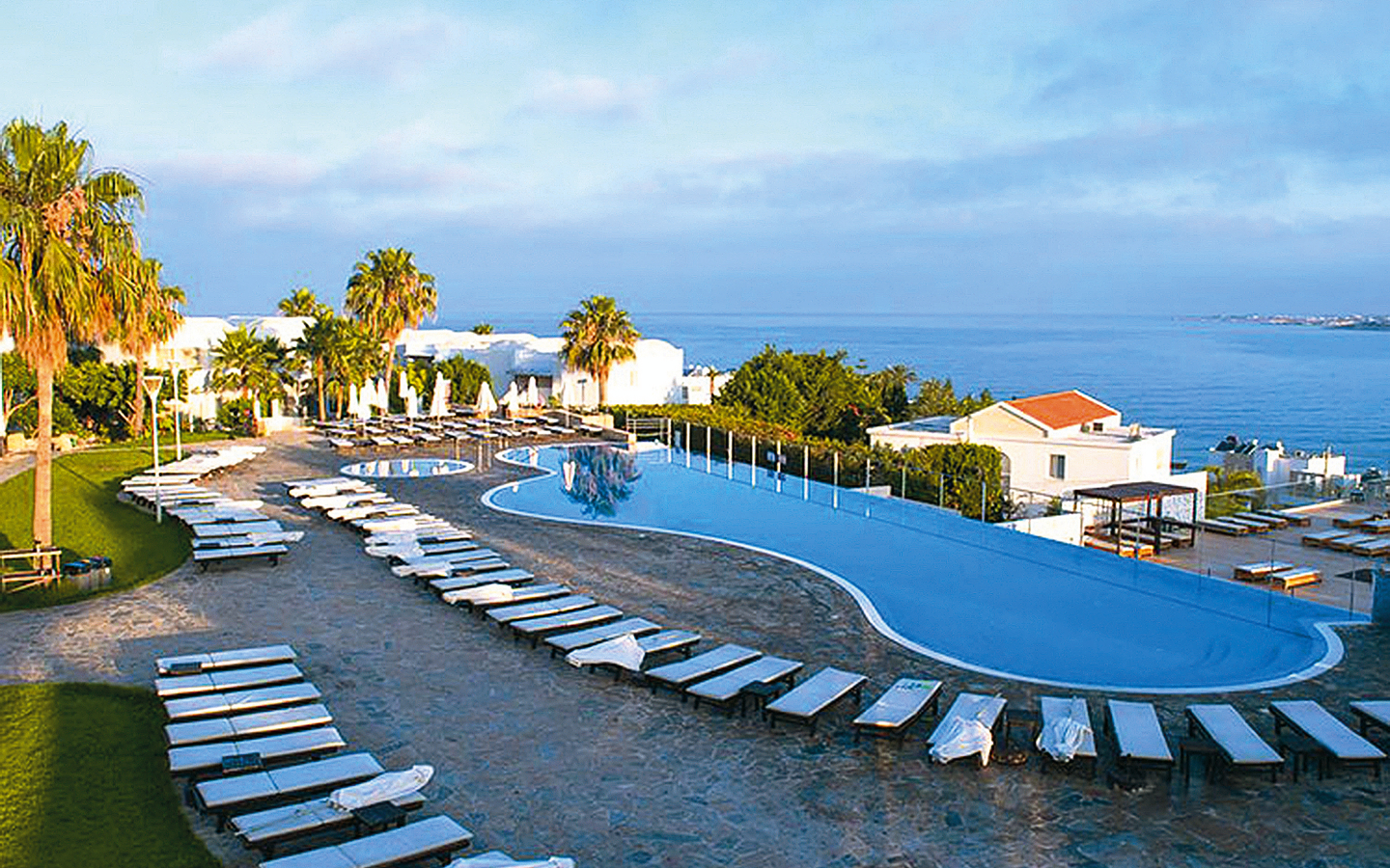 Hotel-Pool mit Liegestühlen und Meerblick bei Sonnenuntergang.