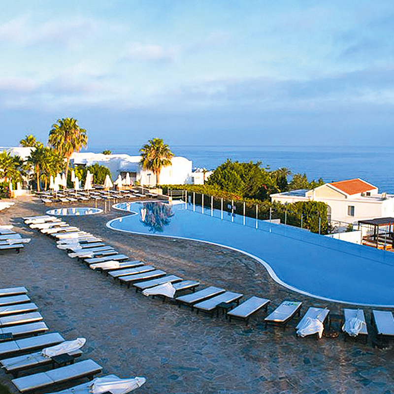 Hotel-Pool mit Liegestühlen und Meerblick bei Sonnenuntergang.