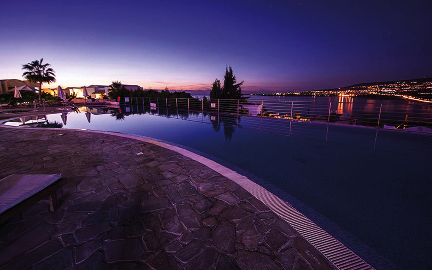Infinity-Pool bei Sonnenuntergang mit Blick auf Küste und Lichter der Stadt.