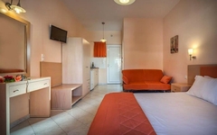 Modernes Hotelzimmer mit Bett, Sofa und kleinem Küchenbereich in warmen Farbtönen.