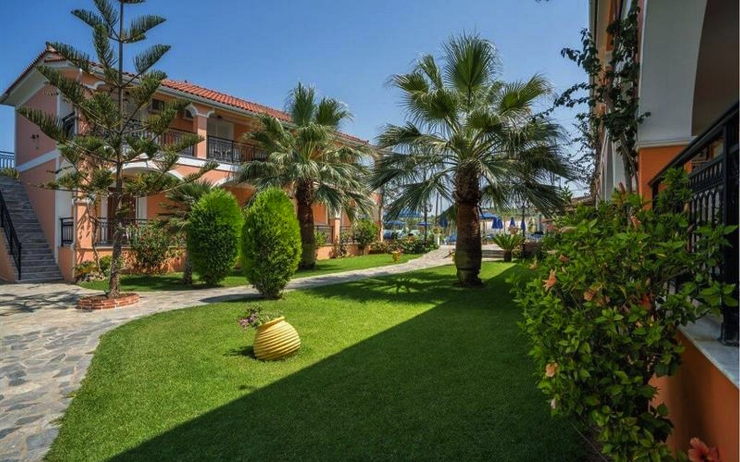 Gartenbereich eines Hotels mit Palmen und gepflegtem Rasen bei Sonnenschein.