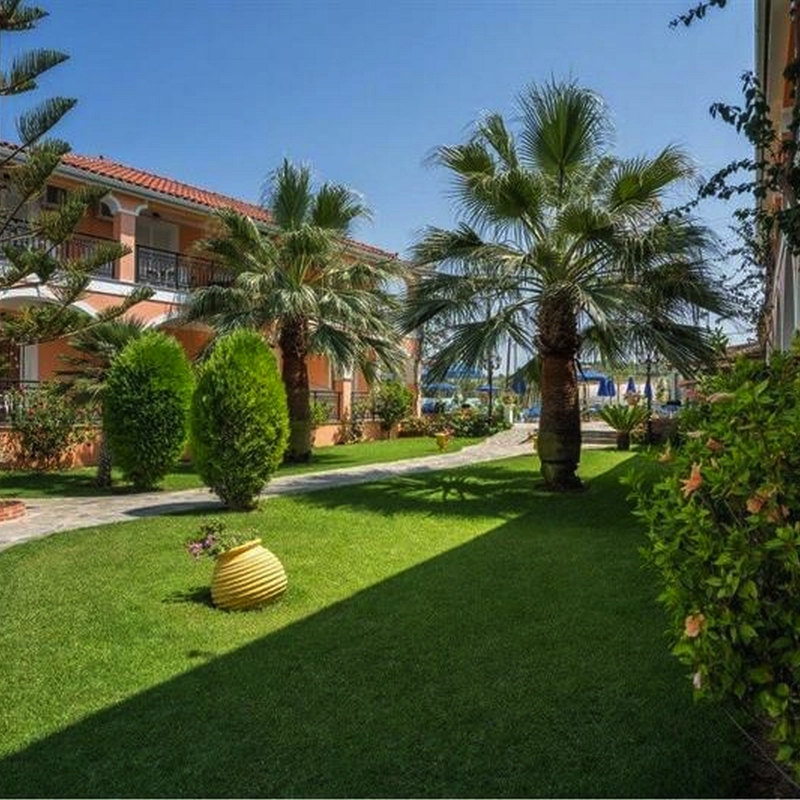 Gartenbereich eines Hotels mit Palmen und gepflegtem Rasen bei Sonnenschein.