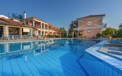 Poolbereich eines Hotels mit blauem Wasser und umliegenden Gebäuden bei sonnigem Wetter.