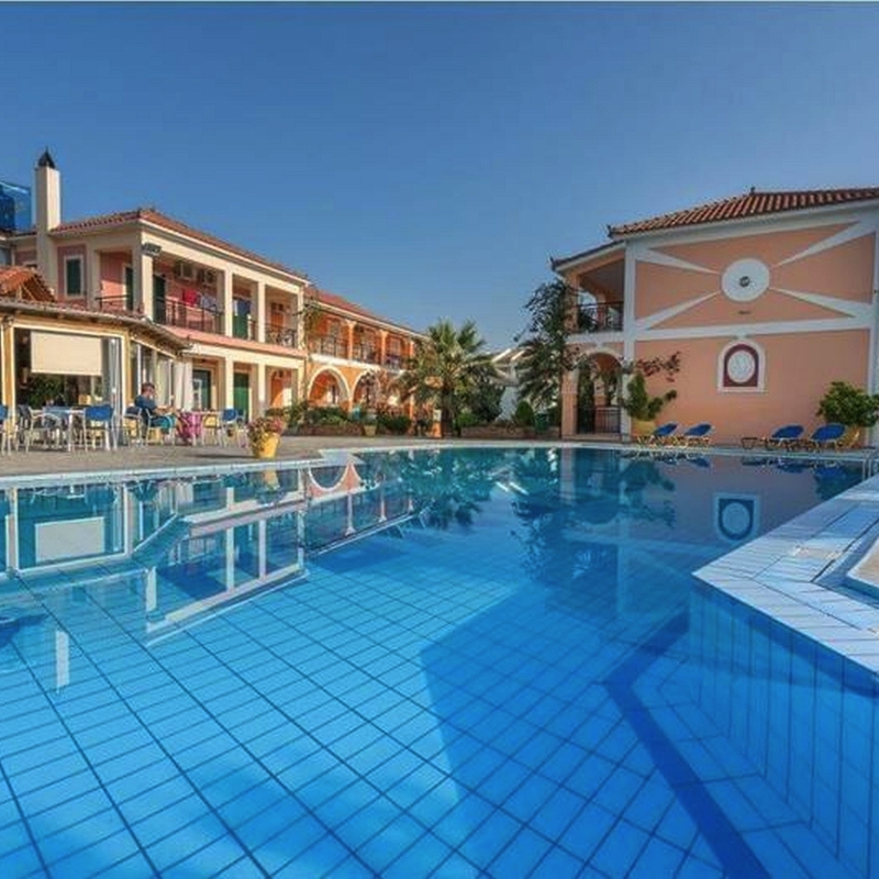 Poolbereich eines Hotels mit blauem Wasser und umliegenden Gebäuden bei sonnigem Wetter.