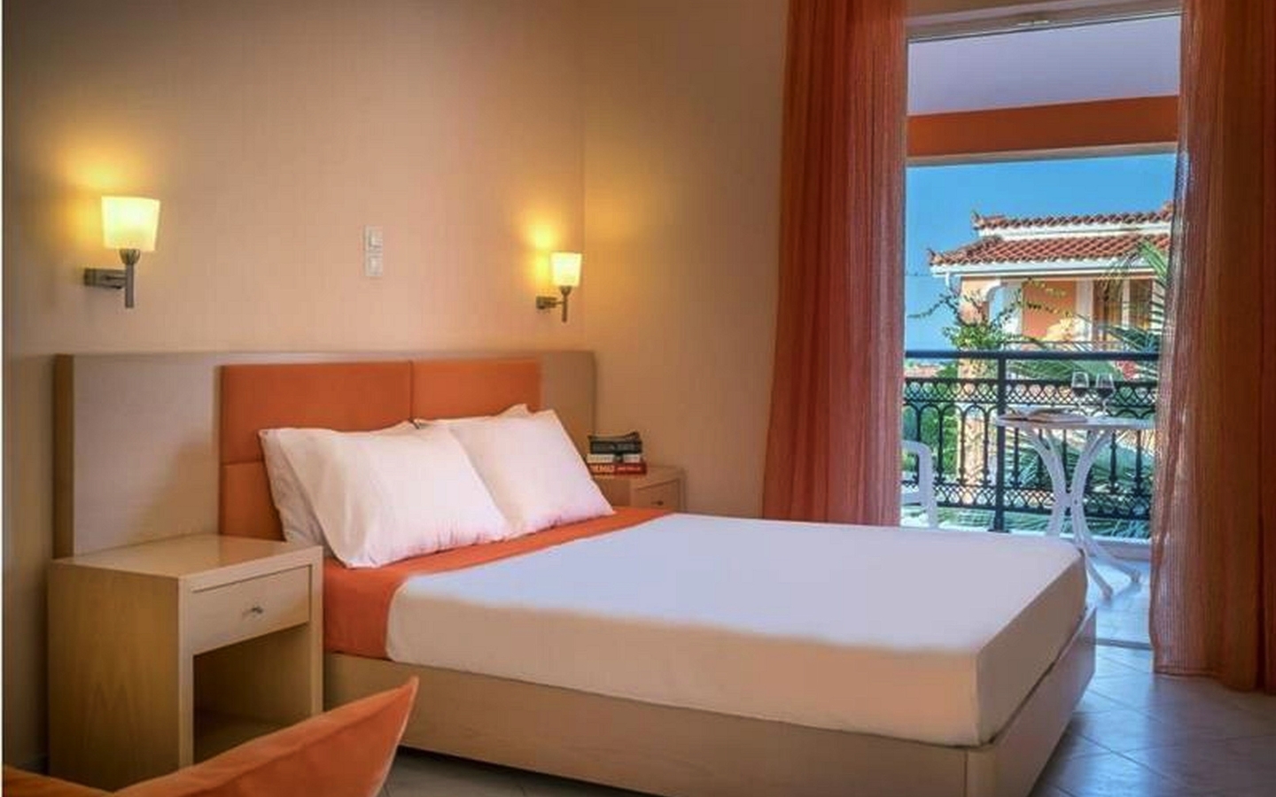 Hotelzimmer mit Doppelbett, Balkon und Blick auf ein traditionelles Haus in Zakynthos, Griechenland.