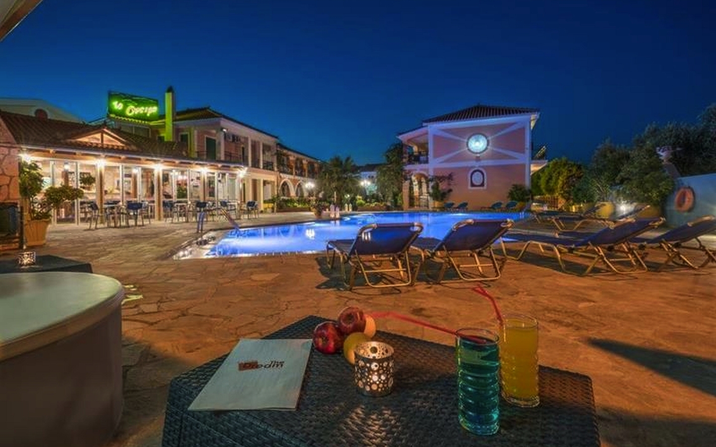 Hotelpool bei Nacht mit Liegestühlen und beleuchteten Gebäuden im Hintergrund.