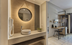 Hotelzimmer mit Waschbecken, Spiegel, Schreibtisch und Regalen.