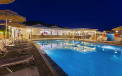 Beleuchteter Hotelpool bei Nacht mit Liegestühlen und Sonnenschirmen