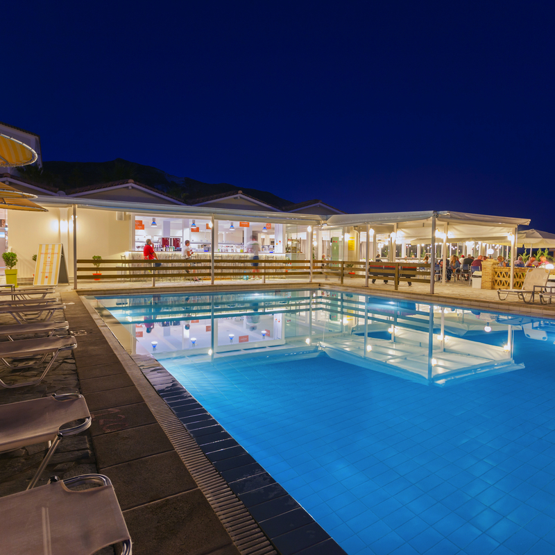 Beleuchteter Hotelpool bei Nacht mit Liegestühlen und Sonnenschirmen