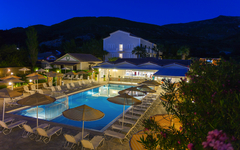 Hotelpool bei Dämmerung mit Liegestühlen in Griechenland, umgeben von Bergen.