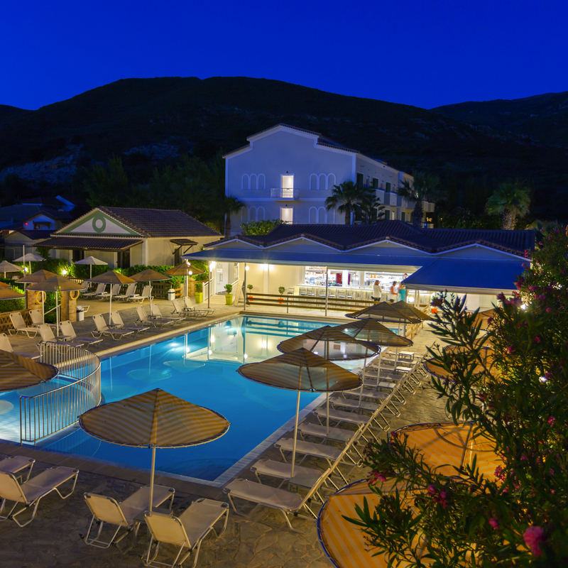 Hotelpool bei Dämmerung mit Liegestühlen in Griechenland, umgeben von Bergen.