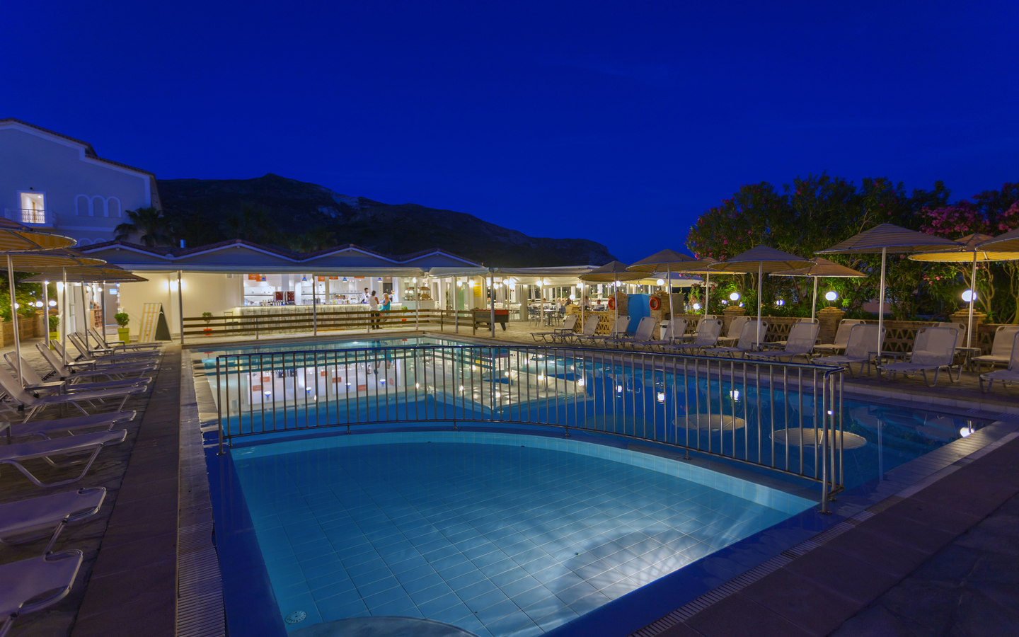 Außenpool im Hotel Cavo d'Oro bei Nacht, umgeben von Sonnenliegen und Schirmen.