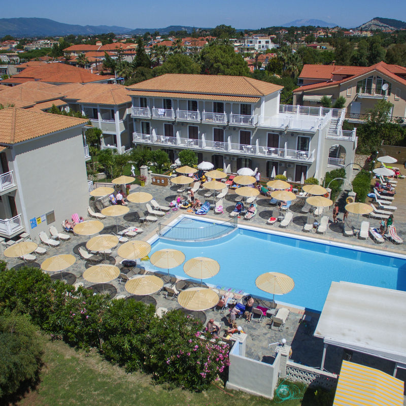 Hotelanlage mit Pool und Sonnenliegen in Griechenland, umgeben von grüner Landschaft.