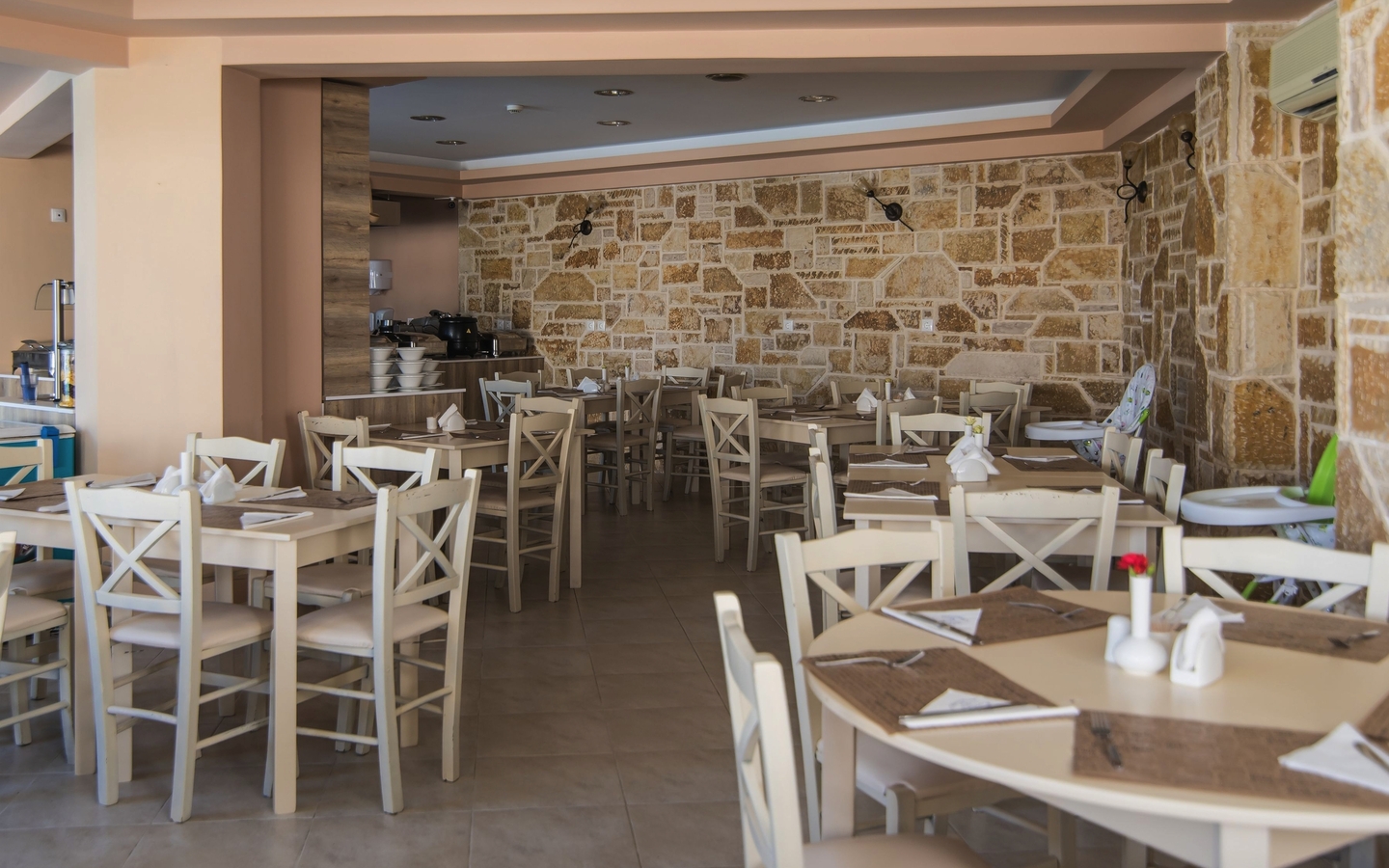 Heller Speisesaal mit hellen Holztischen und Stühlen, Steinwand im Hintergrund.