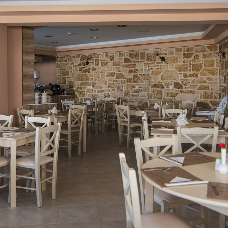 Heller Speisesaal mit hellen Holztischen und Stühlen, Steinwand im Hintergrund.