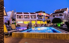 Hotelpool bei Abenddämmerung, umgeben von Liegestühlen und Gebäuden.