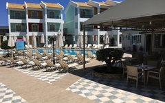 Hotelpoolbereich mit Liegestühlen und Sonnenschirmen vor mehrstöckigem Gebäude.