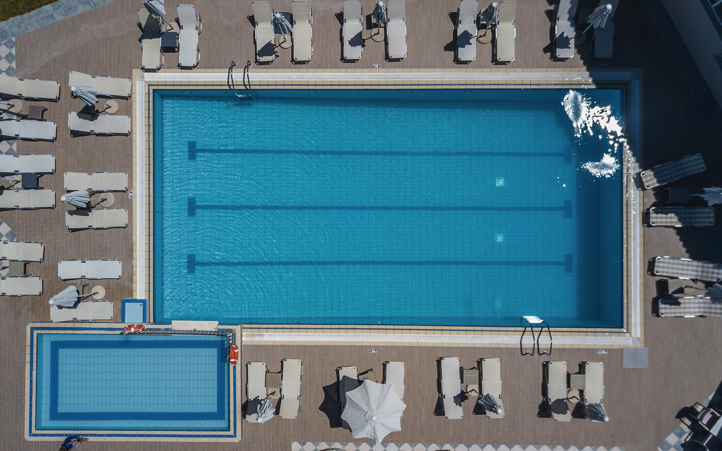 Luftaufnahme eines großen rechteckigen Swimmingpools mit Liegestühlen.