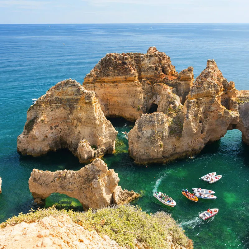Boote im türkisfarbenen Meer vor der felsigen Küste von Lagos, Algarve.