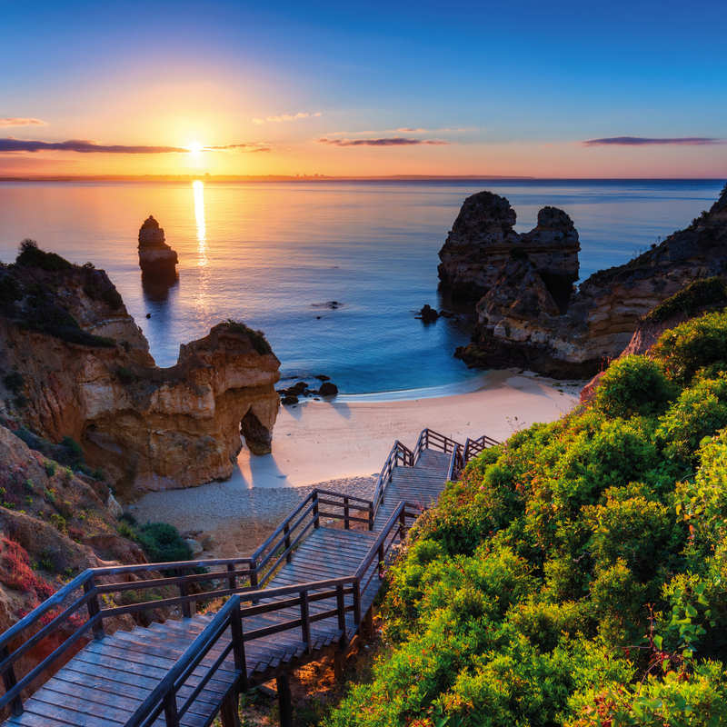 Strand mit Treppe und Felsen bei Sonnenuntergang an der Algarve, Portugal.
