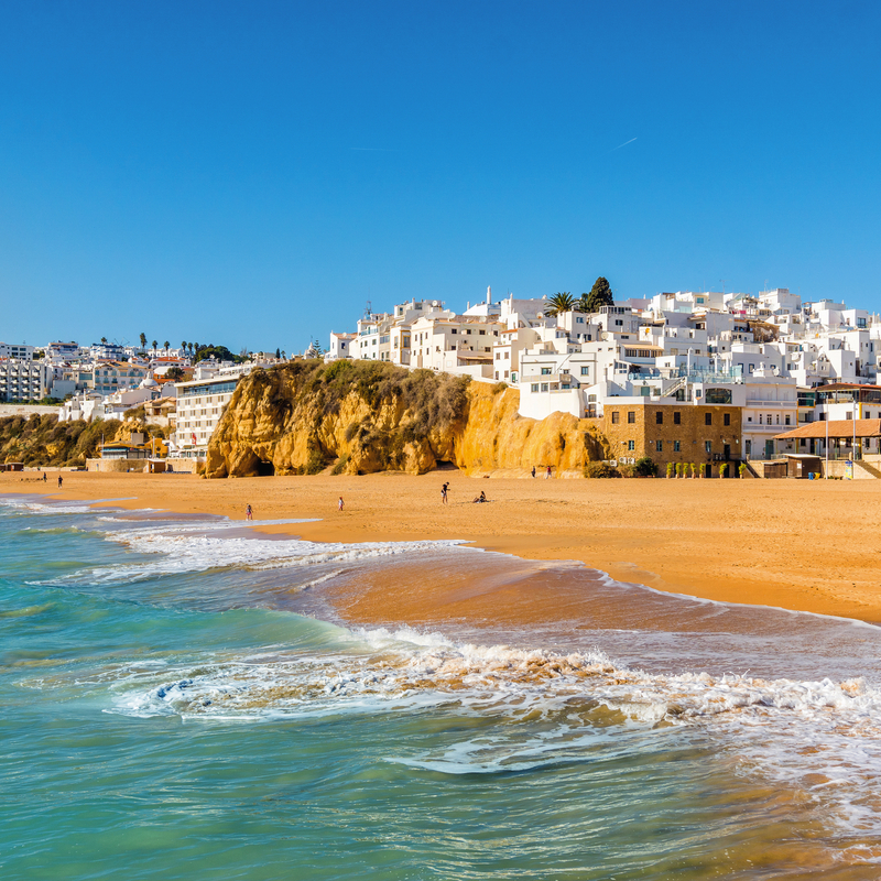 Küstenstadt mit weißen Häusern und Sandstrand am blauen Meer.
